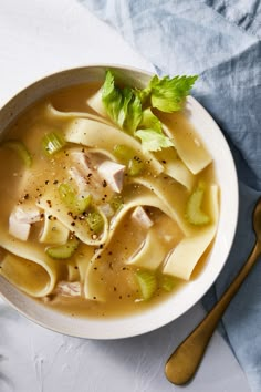 a bowl of soup with noodles, celery and meat in it next to a spoon