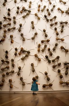 a woman standing in front of a wall covered with lots of small brown balls and needles