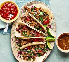 several tacos on a plate with salsa and guacamole next to it