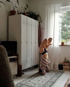 a young boy is doing a handstand in front of a white cabinet and window