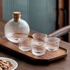 a wooden tray topped with four glasses and a vase filled with nuts on top of it