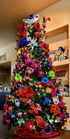 a brightly colored christmas tree with decorations on it's top and bottom branches, in a living room