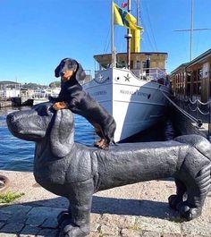 a statue of a dog sitting on the back of a dachshund in front of a boat