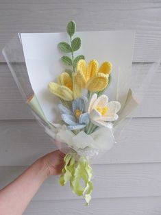 a hand holding a bouquet of flowers on top of a white table next to a wooden wall