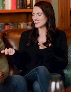 a woman sitting on top of a brown couch talking to someone