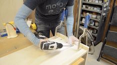 a man working on a piece of wood in his workshop with tools and supplies around him