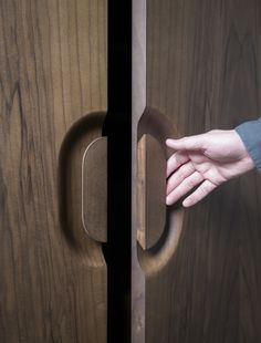 a person's hand reaching into a wooden door with a handle on the side