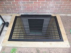 a metal grate sitting on the ground next to a brick wall