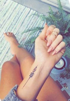 a woman's arm with a tattoo on it and a fern plant behind her