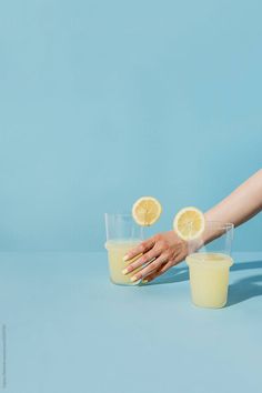 a woman's hand reaching for two glasses of lemonade on a blue background