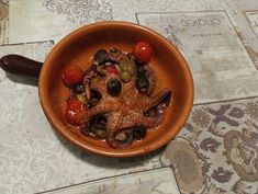 an octopus dish with tomatoes, olives and peppers in a bowl on a table