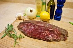 a piece of meat sitting on top of a wooden cutting board next to garlic and lemons