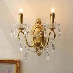 a gold wall light with two lights on each side and crystal drops hanging from it