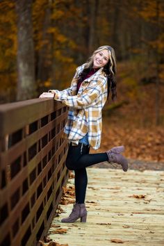 a beautiful young woman leaning on a wooden fence in the fall leaves with her legs crossed