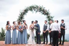 a group of people standing around each other in front of a wedding arch with flowers