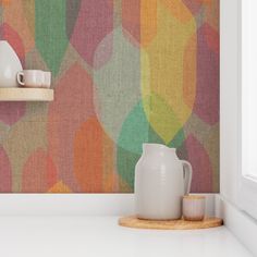 a white vase sitting on top of a counter next to a wall covered in multicolored circles