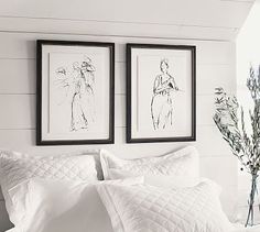 two framed pictures hang on the wall above a bed with white linens and pillows