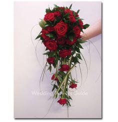 a bouquet of red roses is being held by someone's hand in front of a white wall