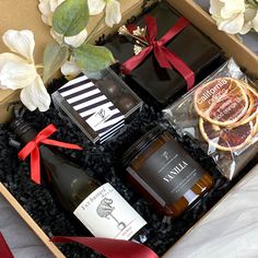 an open gift box containing two bottles of wine and orange slices, with flowers in the background