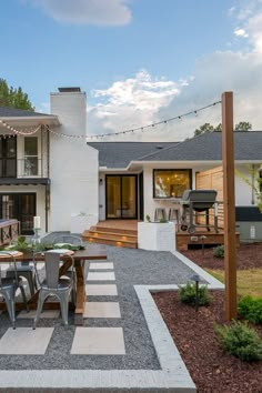 an outdoor dining table and chairs in front of a white house with string lights on the roof