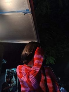 a woman wearing a red and white striped sweater covering her face while standing outside at night