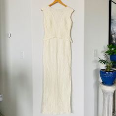 a white dress hanging on a wall next to a potted plant and blue vase