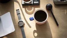 a cup of coffee sits next to a watch and other items on a table top