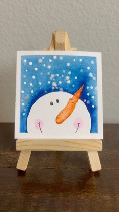 an easel with a painting of a snowman holding a carrot on it's head