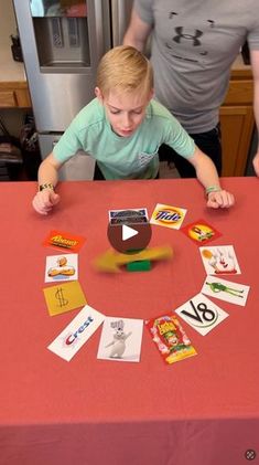 a young boy sitting at a red table with cards and magnets in front of him