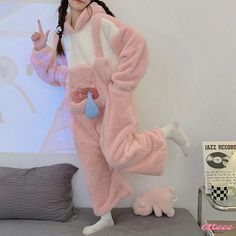 a girl in a pink animal onesie standing on a bed with her hands up