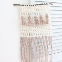 a crocheted wall hanging with tassels hangs on a window sill