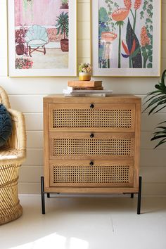 a wicker dresser with two pictures on the wall behind it