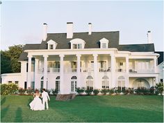 two people walking in front of a large white house