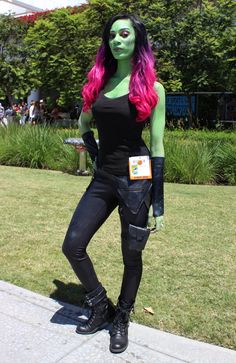 a woman with pink hair and green makeup is dressed in black leather pants and boots