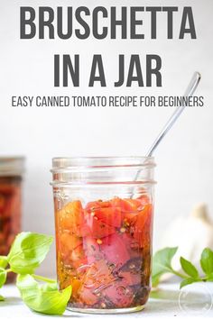 a glass jar filled with sliced tomatoes and basil leaves on top of a white table