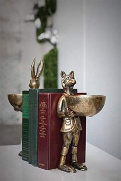 a bookend with a gold rabbit holding a bowl on it's back and two books in the background