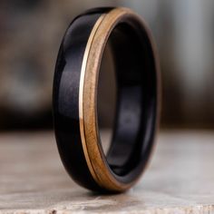 a black and gold wedding ring on top of a wooden table with wood inlays