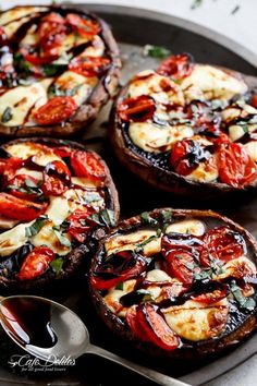 four baked pizzas with tomatoes and cheese on a plate next to a spoon,