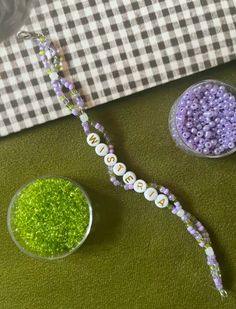 two bowls filled with green and purple beads next to each other on a checkered table cloth