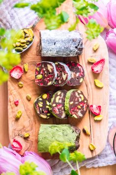 an assortment of sushi on a wooden board next to pink flowers and green leaves