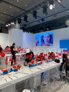 a group of people sitting at tables with red flowers in vases on the table