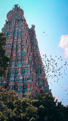 many birds are flying in the sky near a tall building that has ornate designs on it