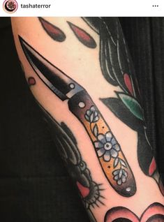 a tattoo with a knife and flowers on it's arm that is next to a heart