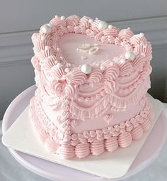 a large pink cake with white decorations on it's sides and a heart shaped frosting decoration