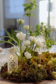 a table topped with white flowers and greenery on top of a moss covered surface