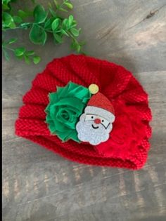 a red knitted hat with a green flower and santa's face on it