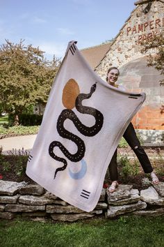 a woman holding up a white towel with a snake on it in front of a building