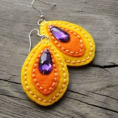 two yellow and orange felt earrings with purple beads on wooden table next to wood plank