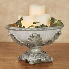 three lit candles sit in a silver bowl with ivy and leaves on the rim, surrounded by greenery