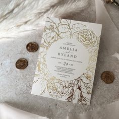 a white and gold wedding card with roses on it next to two coins, one for the bride